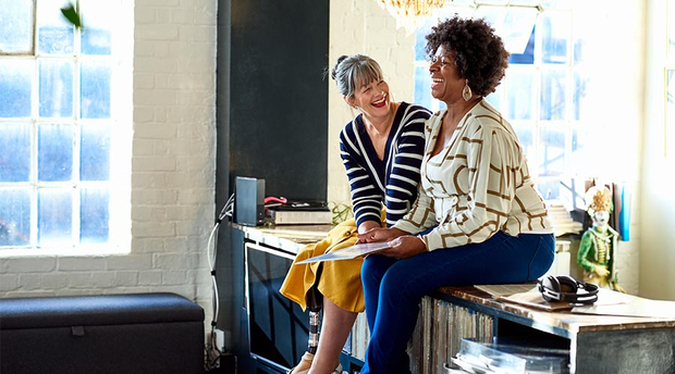 Two women sitting on sideboard laughing together