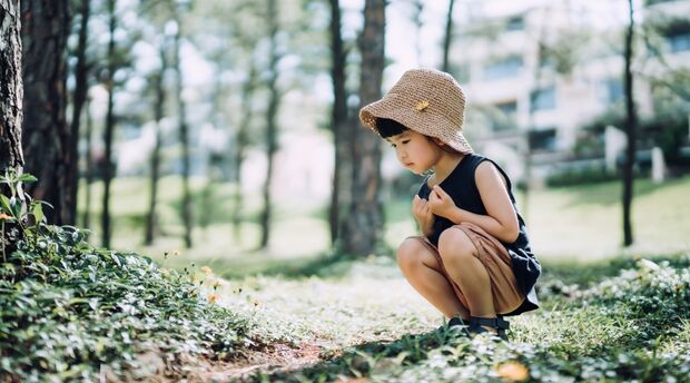 A little girl with straw hat looking at flowers in the woods